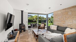 A modern living room with a fireplace, a flat-screen TV, and a stone wall. - Stylish 4‑Bedroom St Andrews Cottage with Private Garden, Parking & Walk to South Street (St. Andrews)