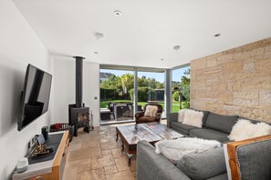 A modern living room with a fireplace, a flat-screen TV, and a stone wall. - Stylish 4‑Bedroom St Andrews Cottage with Private Garden, Parking & Walk to South Street (St. Andrews)