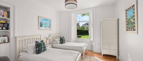 Ein Schlafzimmer mit zwei Einzelbetten, einem Kleiderschrank, einem Bücherregal und einem Fenster mit Gartenblick.