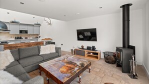 A modern living room with a sofa, coffee table, fireplace, and kitchen area. - Stylish 4‑Bedroom St Andrews Cottage with Private Garden, Parking & Walk to South Street (St. Andrews)