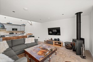 A modern living room with a sofa, coffee table, fireplace, and kitchen area. - Stylish 4‑Bedroom St Andrews Cottage with Private Garden, Parking & Walk to South Street (St. Andrews)