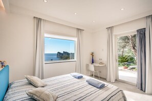 Un dormitorio con cama, escritorio y vista al mar.
