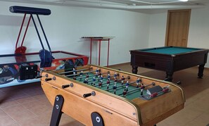 A room with a foosball table, a pool table, and a red and blue table tennis table.