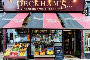 A storefront with a sign reading "PECKHAM'S VINTNERS & VICTUALLERS" and a variety of fresh produce displayed outside. - Crown Gardens (Glasgow)