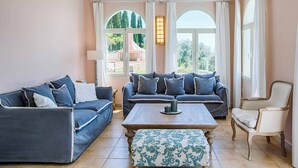 A living room with a blue sofa set, a white armchair, and a patterned ottoman. - Villa Agapi - Four Bedroom Villa, Sleeps 8 (Lefkada)