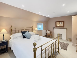 A bedroom with a bed, nightstands, a chair, a fireplace, and a window.