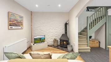 A cozy living room with a stone wall, a fireplace, a TV, and a staircase.