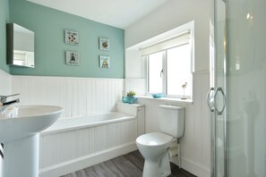 Une salle de bain avec un lavabo blanc, une baignoire, des toilettes et une cabine de douche en verre.