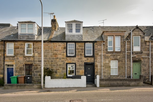 A row of stone houses with multiple windows and doors, some with small balconies, and a street in front. - Elegant 4‑Bedroom Townhouse in Central St Andrews with Garden, Parking & Walk to Old Course (St. Andrews)