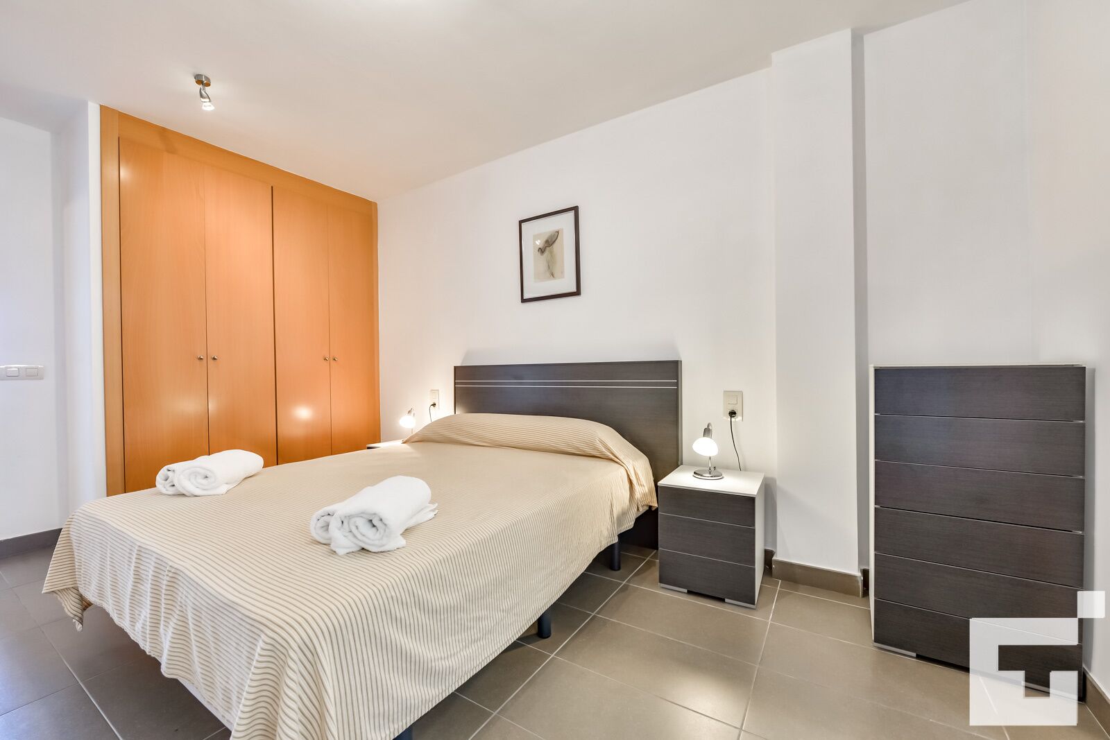 Een moderne hotelkamer met een groot bed, een houten garderobe, een nachtkastje met een lamp en een ingelijst kunstwerk aan de muur.
