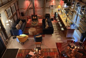 Um interior acolhedor e rústico com lareira de pedra, assentos confortáveis e área de bar com diversos copos e garrafas.