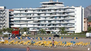 Un hôtel à plusieurs étages doté de balcons, d’une plage avec des transats et offrant une vue dégagée sur la mer.