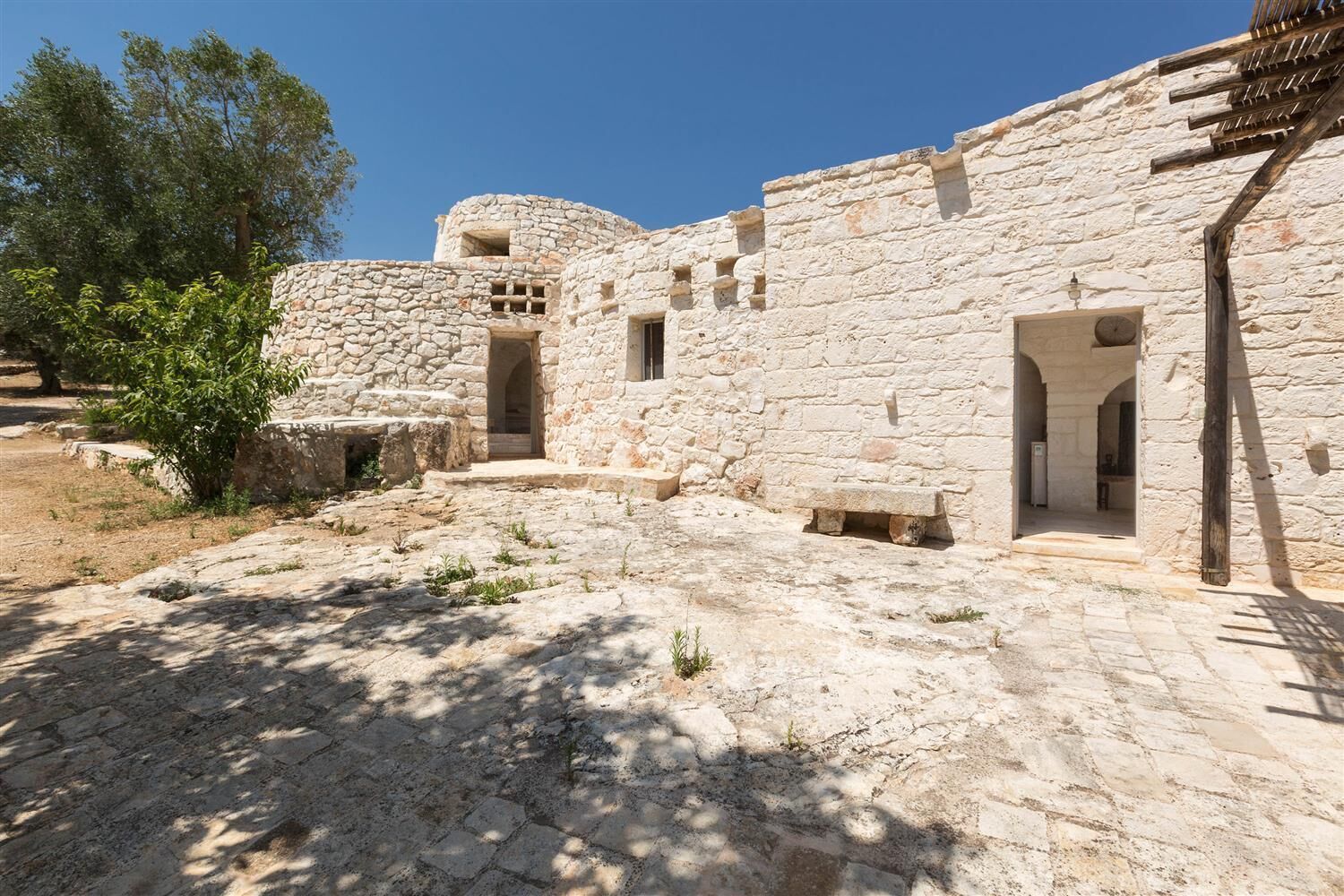 Un bâtiment en pierre doté de nombreuses portes et fenêtres, entouré d’une cour pavée.