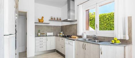 Una cocina moderna con armarios blancos, lavavajillas, estufa y ventana con cortinas.