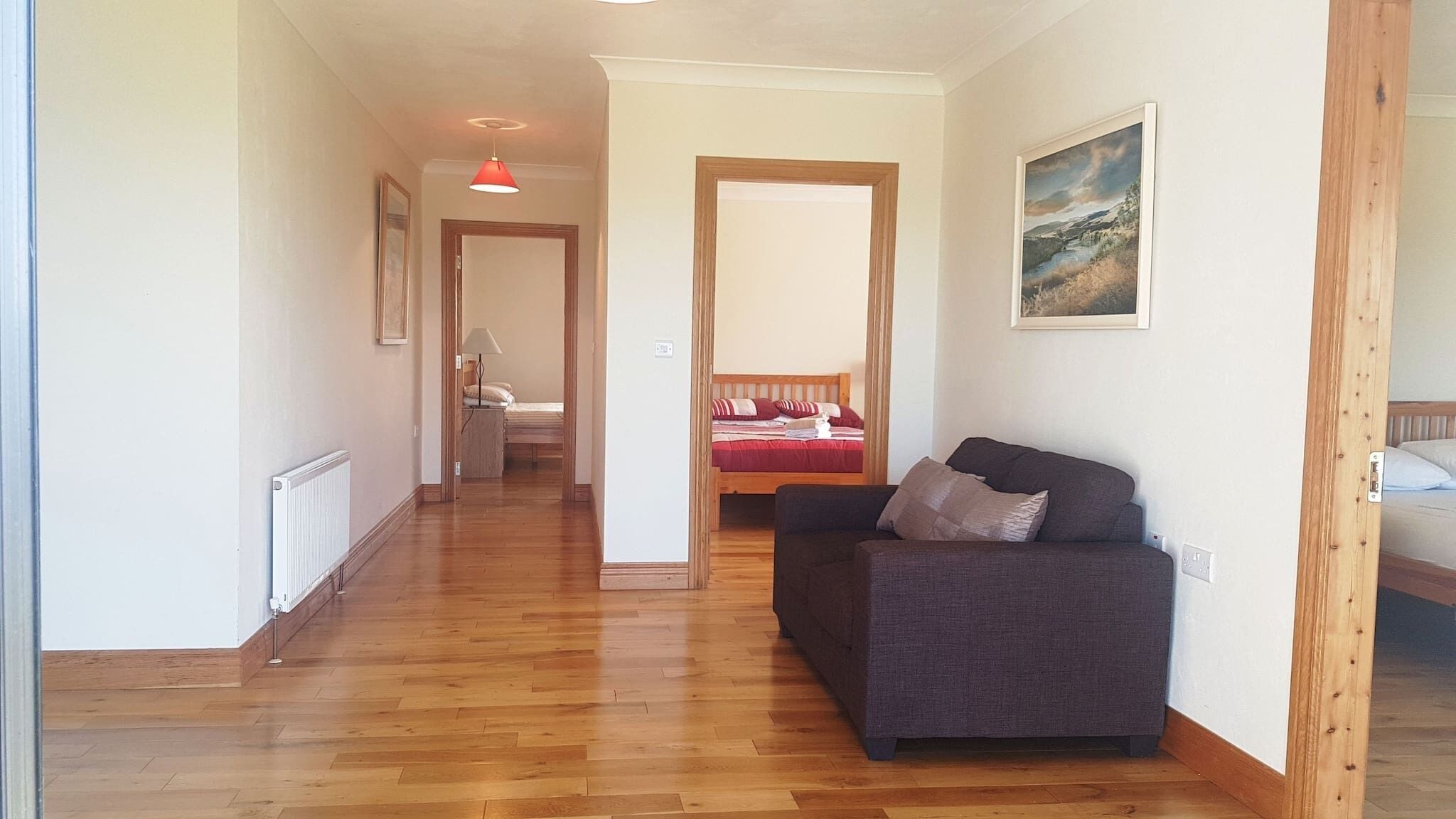 A hallway with wooden flooring leading to a room with a sofa and a bed.