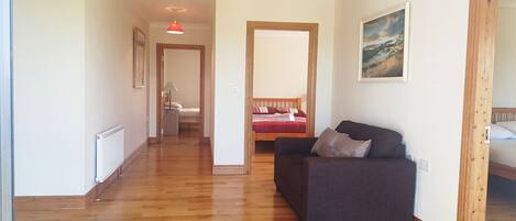 A hallway with wooden flooring leading to a room with a sofa and a bed.