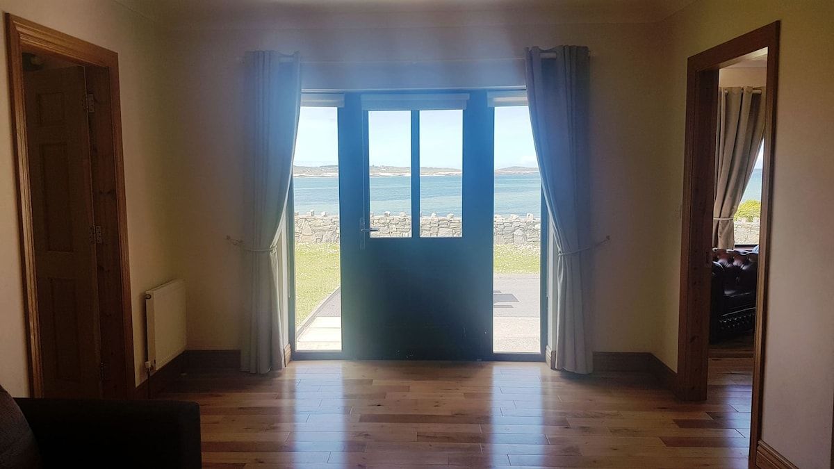 A room with a wooden floor, a door leading outside, and a view of the sea.