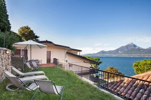 A seaside villa with a terrace, lounge chairs, and a view of the sea and mountains. - Greenery Loft With Lake View (Torri del Benaco)