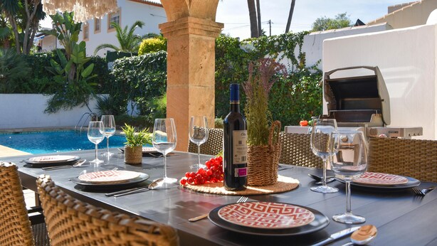 Un espace extérieur aménagé pour les repas, avec une piscine, un barbecue et une bouteille de vin.
