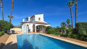 Une villa blanche avec une piscine, entourée de palmiers et de verdure.