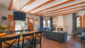 Un salon spacieux avec des poutres apparentes, un coin repas avec une table et des chaises en bois, un canapé et une cheminée.