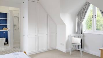 A bedroom with a bed, a white wardrobe, a window with curtains, and a bathroom with a shower.