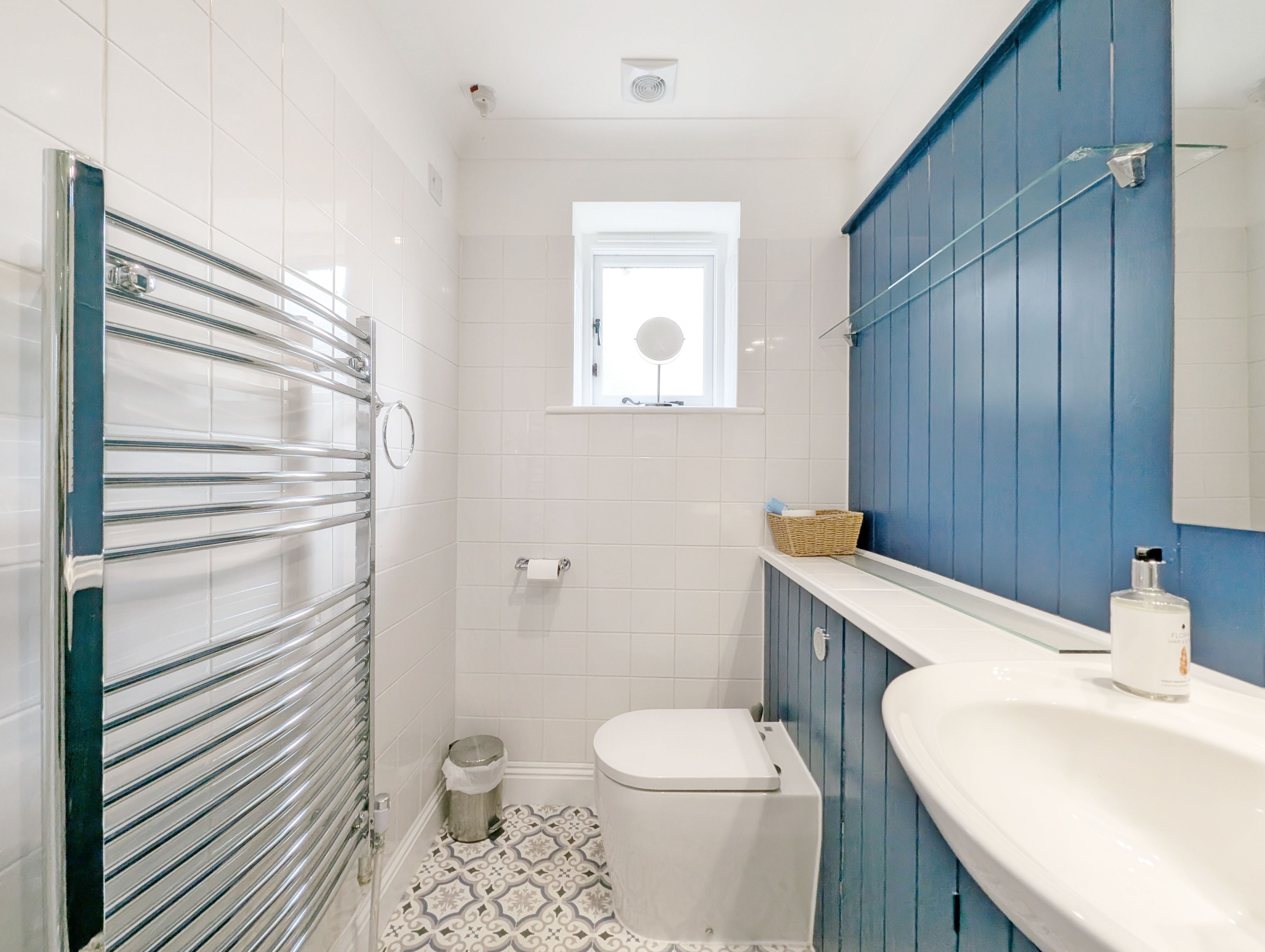 A compact bathroom with a toilet, a small window, a mirror, a sink, and a shower area.