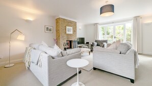 A modern living room with a brick fireplace, two grey sofas, a white coffee table, and a floor lamp. - Old Lock Cottage, Birdham (Chichester)