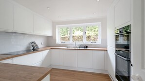 A modern kitchen with white cabinets, a wooden countertop, a built-in oven, and a window with a view of greenery. - Old Lock Cottage, Birdham (Chichester)