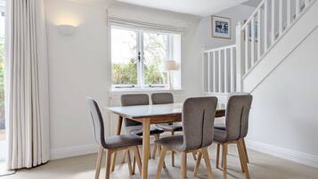 A dining area with a table and chairs, a window with curtains, a lamp, and a staircase.