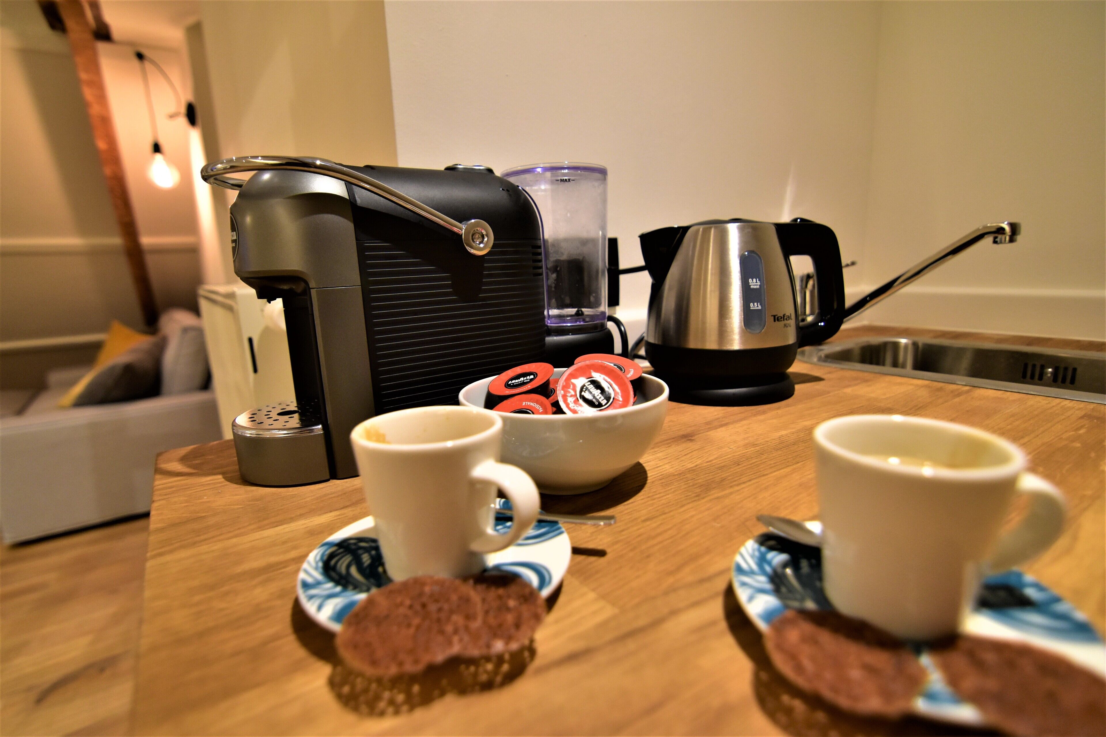 A kitchen counter with a coffee maker, a kettle, and a bowl of coffee pods.