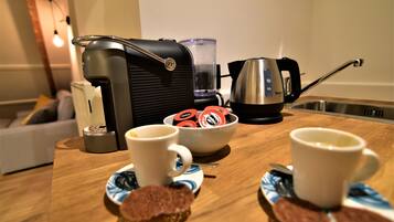 A kitchen counter with a coffee maker, a kettle, and a bowl of coffee pods.