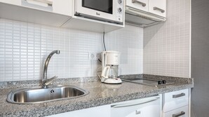 Eine Küche mit weißen Schränken, einer Edelstahl-Spüle, einer Kaffeemaschine und einer Mikrowelle.
