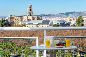 A balcony with a table set for breakfast, overlooking a cityscape with historic buildings and a prominent tower. - Susana - Holiday home in Malaga (Málaga)