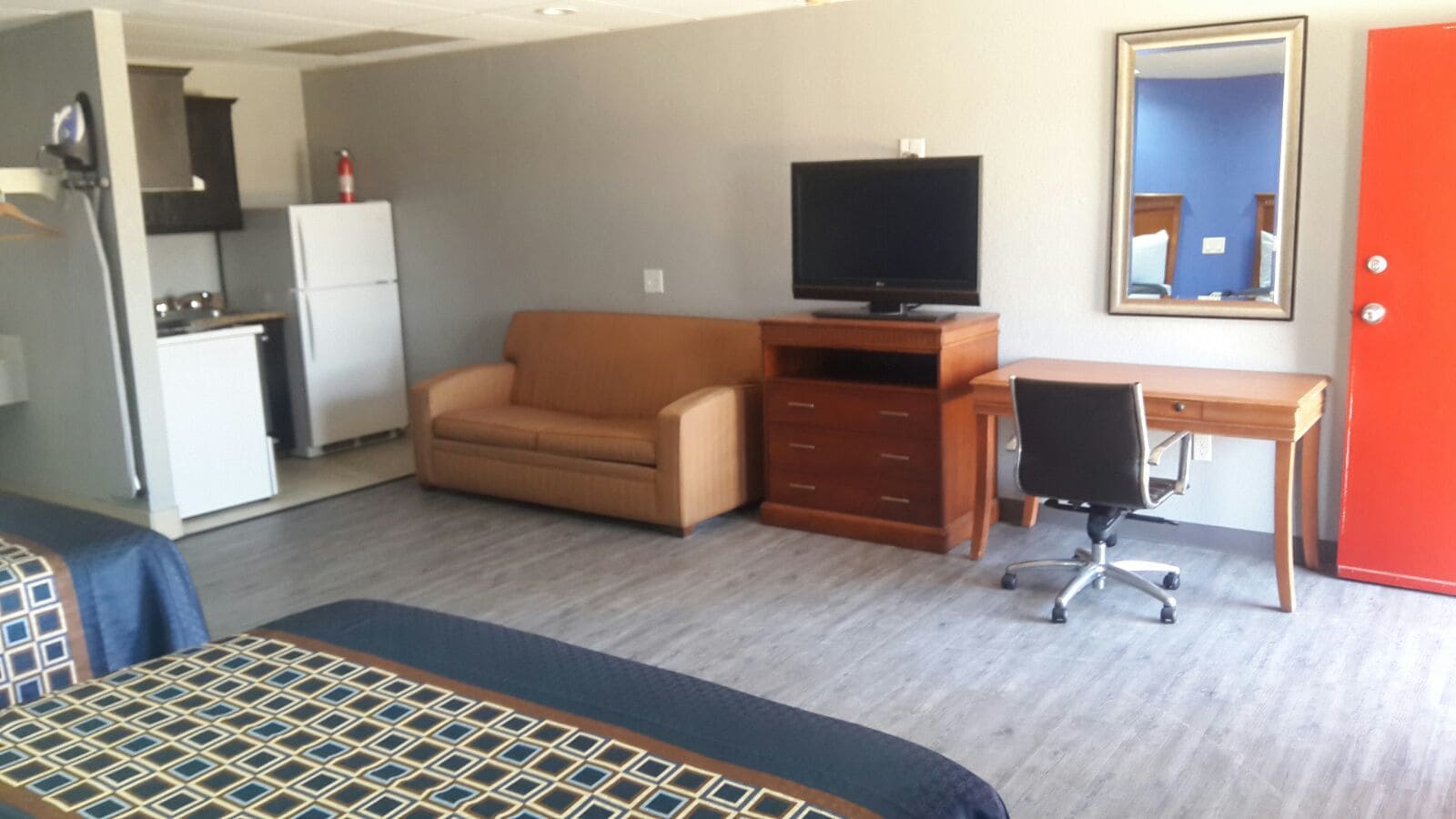 Habitación de hotel con cama, sofá, escritorio y silla, televisor, armario y puerta.