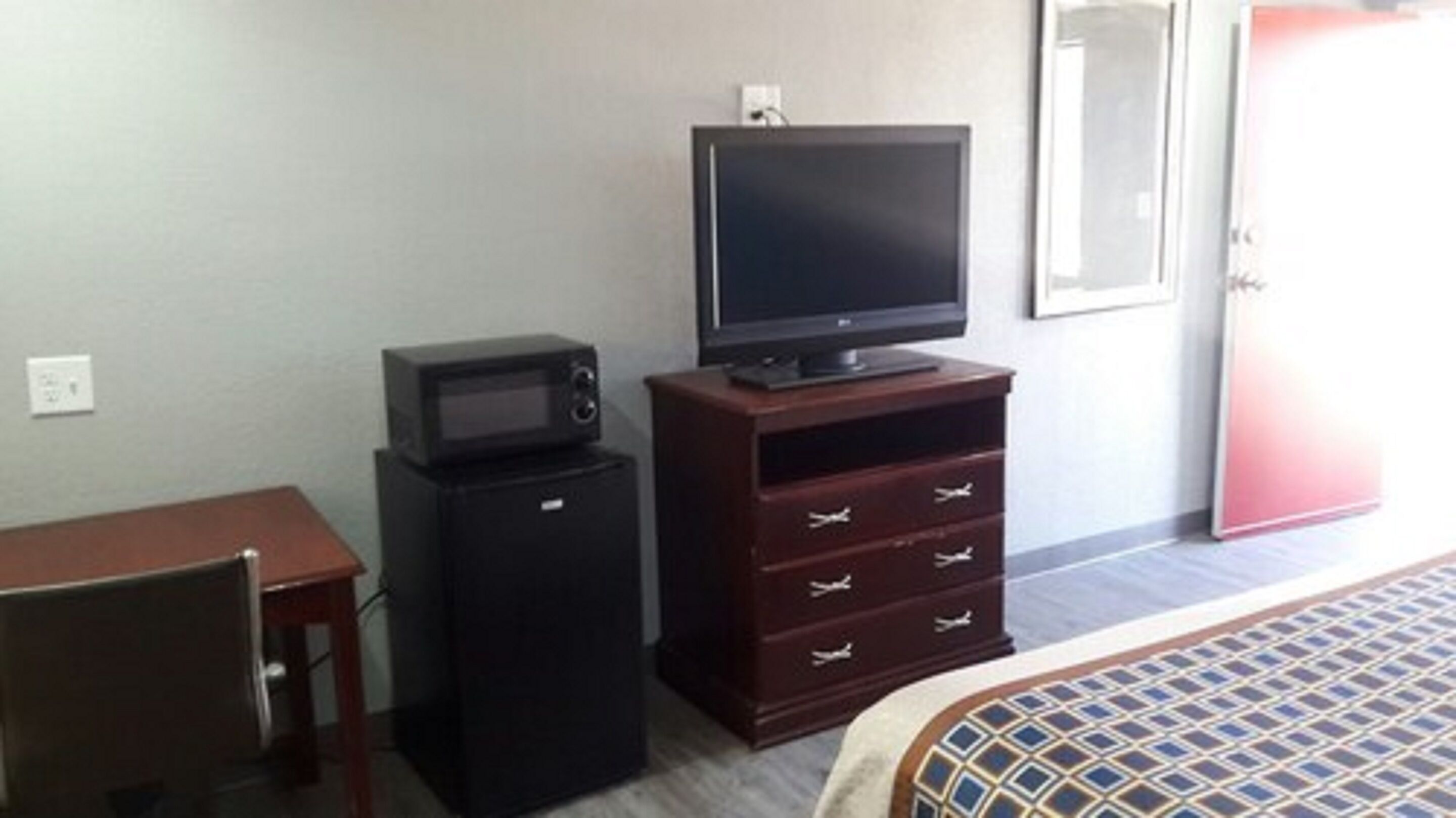 Habitació d'hotel amb un llit, una televisió sobre una cómoda de fusta, microones i una petita taula d'escriptori amb una cadira.