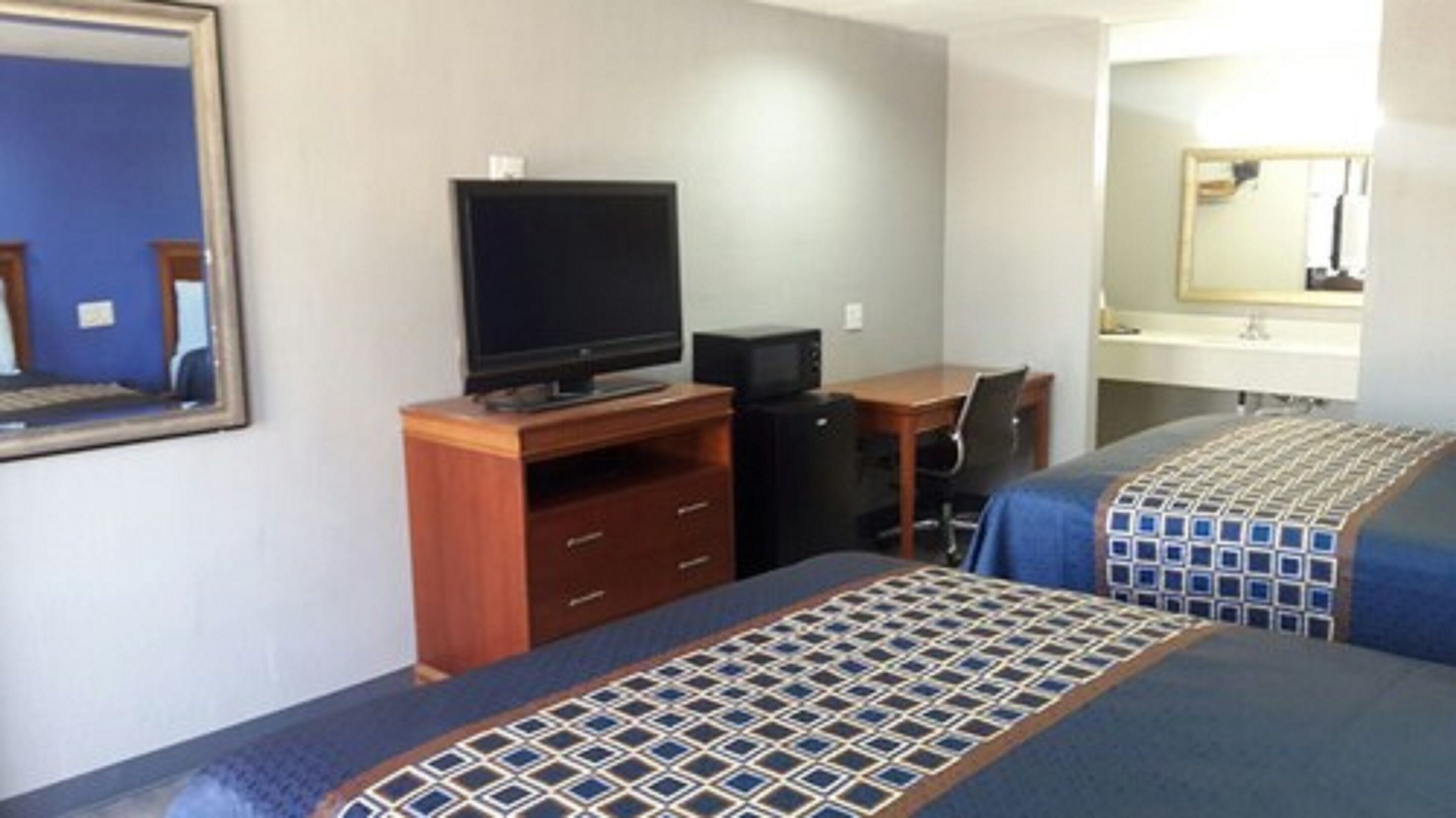 A hotel room with a bed, a desk, a television, and a mirror.