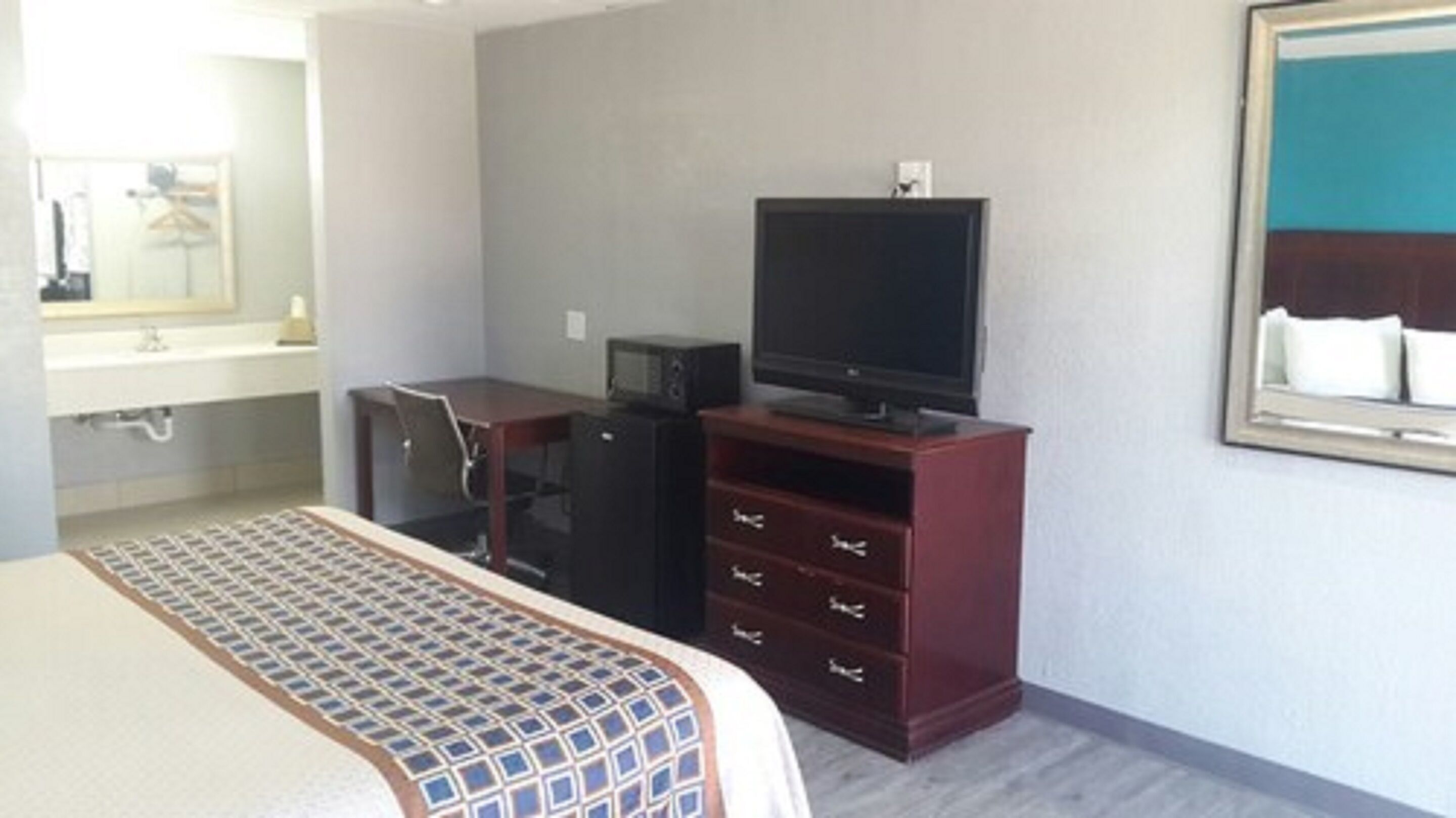 Une chambre d’hôtel comprenant un lit, un bureau avec une télévision, une commode et une salle de bain avec un lavabo et un miroir.