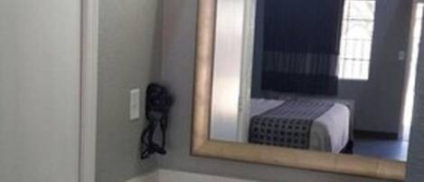 A bathroom with a white sink, a mirror, a black trash bin, and a door.
