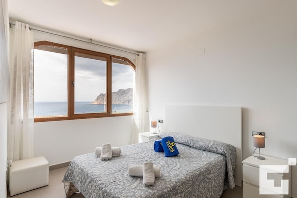 Un dormitorio con un ventanal grande, una cama, una mesita de noche y un buró.
