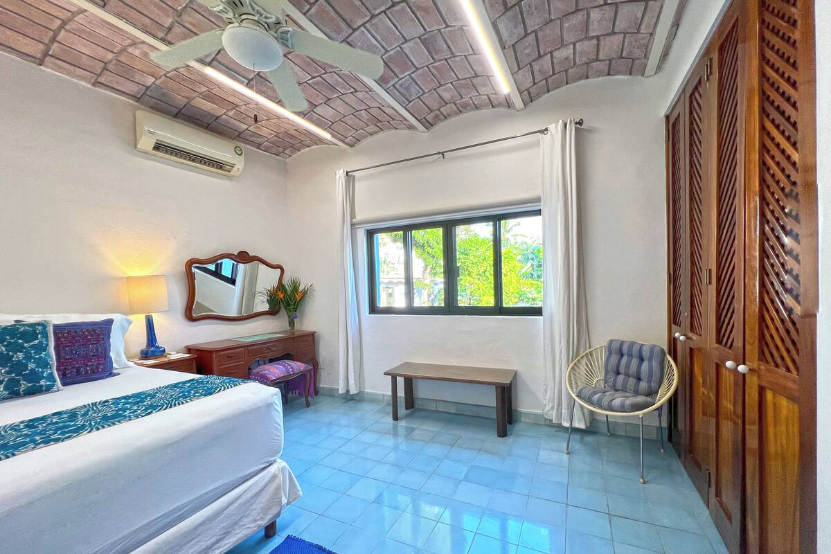 Um quarto com uma cama, escrivaninha, cadeira, janela e ventilador de teto.