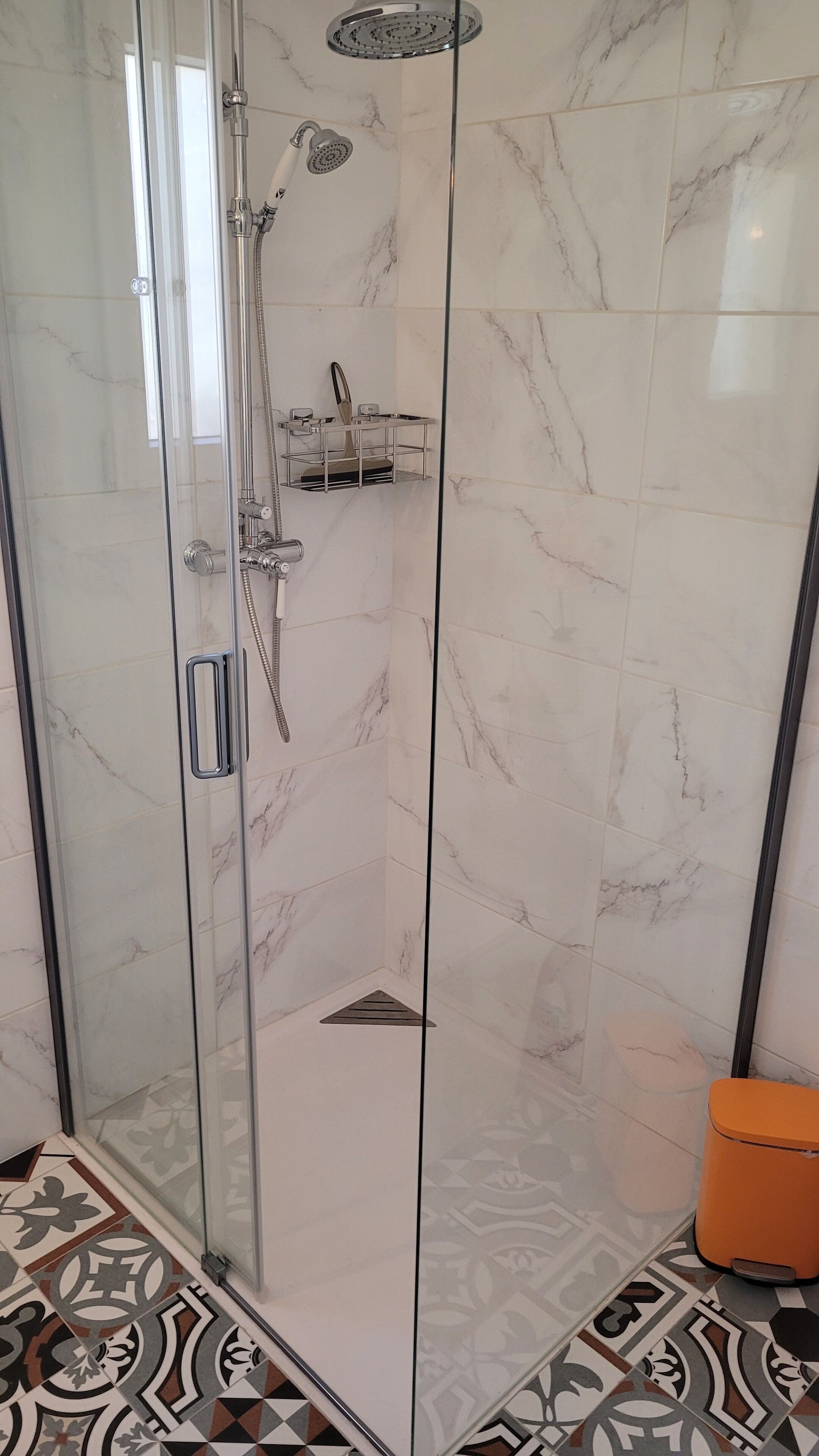 A glass-enclosed shower with a handheld showerhead and a wall-mounted faucet.