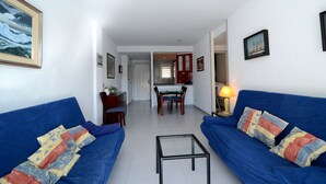 Ein Wohnzimmer mit blauen Sofas, einem Glastisch und einem Essbereich mit Tisch und Stühlen.