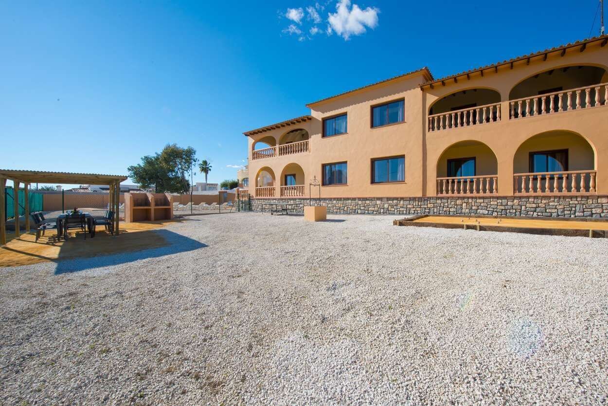 A building with multiple balconies, a covered outdoor seating area, and a gravel courtyard.