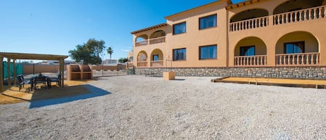 A building with multiple balconies, a covered outdoor seating area, and a gravel courtyard.