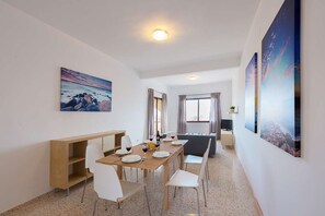 Uma sala de jantar moderna com mesa de madeira, cadeiras brancas e um quadro na parede.