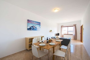 A dining area with a table set for four, chairs, a painting on the wall, and a view through a window.