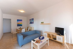 A compact living space with a sofa, a dining table, a TV, and artwork on the walls.