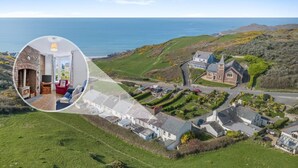 A coastal village with a prominent stone church, a small brick house with a fireplace, and a view of the sea.