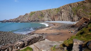 A coastal beach with rocky cliffs, a sandy shore, and a stone wall.